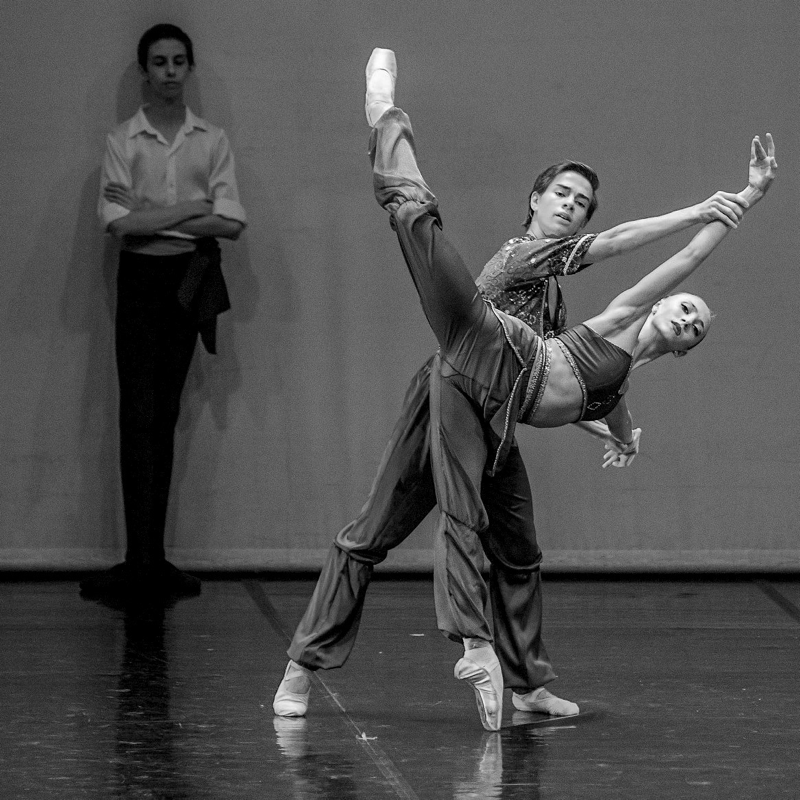 Dois bailarinos ensaiam um pas de deux sob o olhar de uma professora.